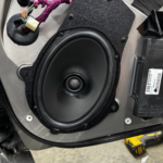 Black car speaker mounted in a vehicle door panel during installation process.