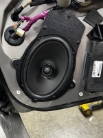 Black car speaker mounted in a vehicle door panel during installation process.