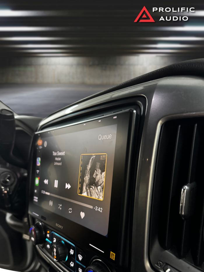 Angled view of Sony XAV-9500ES receiver installed in a 2014-2019 Chevrolet Silverado or GMC Sierra, showing music playback on the screen.