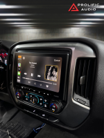 Angled view of the Sony XAV-AX8500 installed in a 2014-2019 Chevrolet Silverado or GMC Sierra, displaying the CarPlay interface with Hozier's "Too Sweet" playing on the screen.