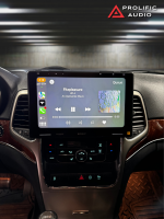 Interior view of a 2011-2013 Jeep Grand Cherokee with the Sony XAV-9500ES radio installed using Prolific Audio's DIY kit, running Apple CarPlay. The screen displays a music player interface with the song "Fitzpleasure" by alt-J from the album "An Awesome Wave," along with album art and playback controls. The factory HVAC controls remain functional below the radio, ensuring a seamless integration.