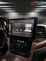 Side-angle view of the interior of a 2011-2013 Jeep Grand Cherokee showcasing the Sony XAV-9500ES radio installed using Prolific Audio's DIY kit. The screen is running Apple CarPlay, displaying the Pandora music interface with the song "Little Lion Man" by Mumford & Sons from the album "Sigh No More," including album art and playback controls. The custom bezel ensures a clean and professional integration with the dashboard, retaining the factory HVAC controls below.