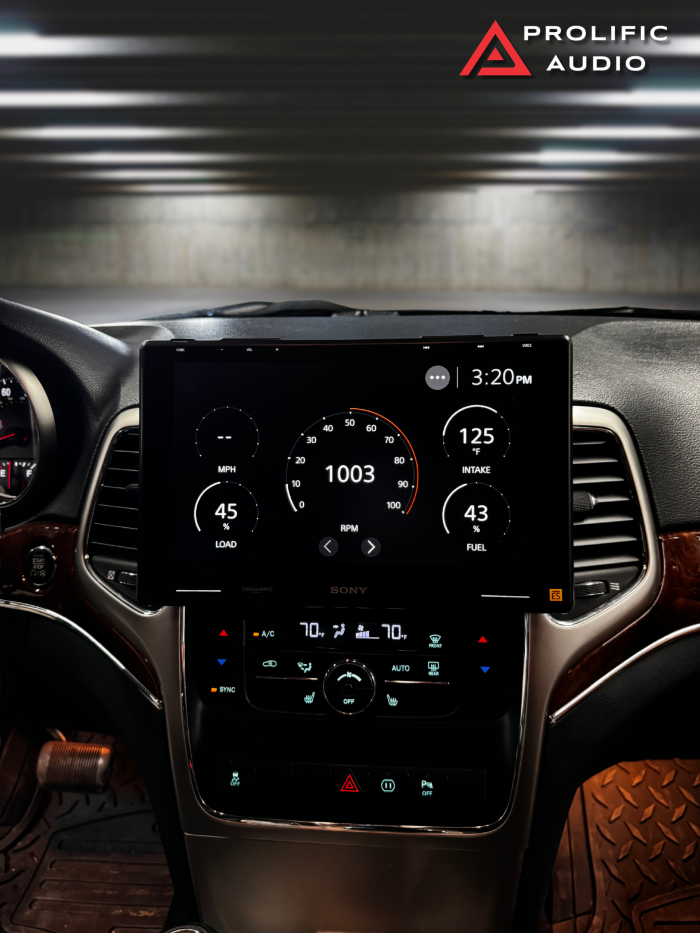 Interior view of a 2011-2013 Jeep Grand Cherokee showcasing the Sony XAV-9500ES radio installed with Prolific Audio's DIY kit. The screen displays real-time vehicle performance data, including speed, engine load, RPM, intake temperature, and fuel level. The custom bezel integrates seamlessly into the dashboard, maintaining the factory HVAC controls below for a clean and professional installation.