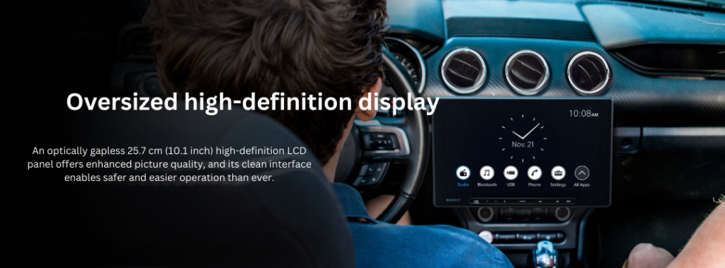 Display showcasing the Sony XAV-AX8500 radio's oversized 10.1-inch high-definition LCD screen installed in a vehicle. The screen highlights its gapless design and clear user interface, with menu options for radio, Bluetooth, USB, phone, settings, and all apps, emphasizing enhanced picture quality and safer, easier operation for drivers.